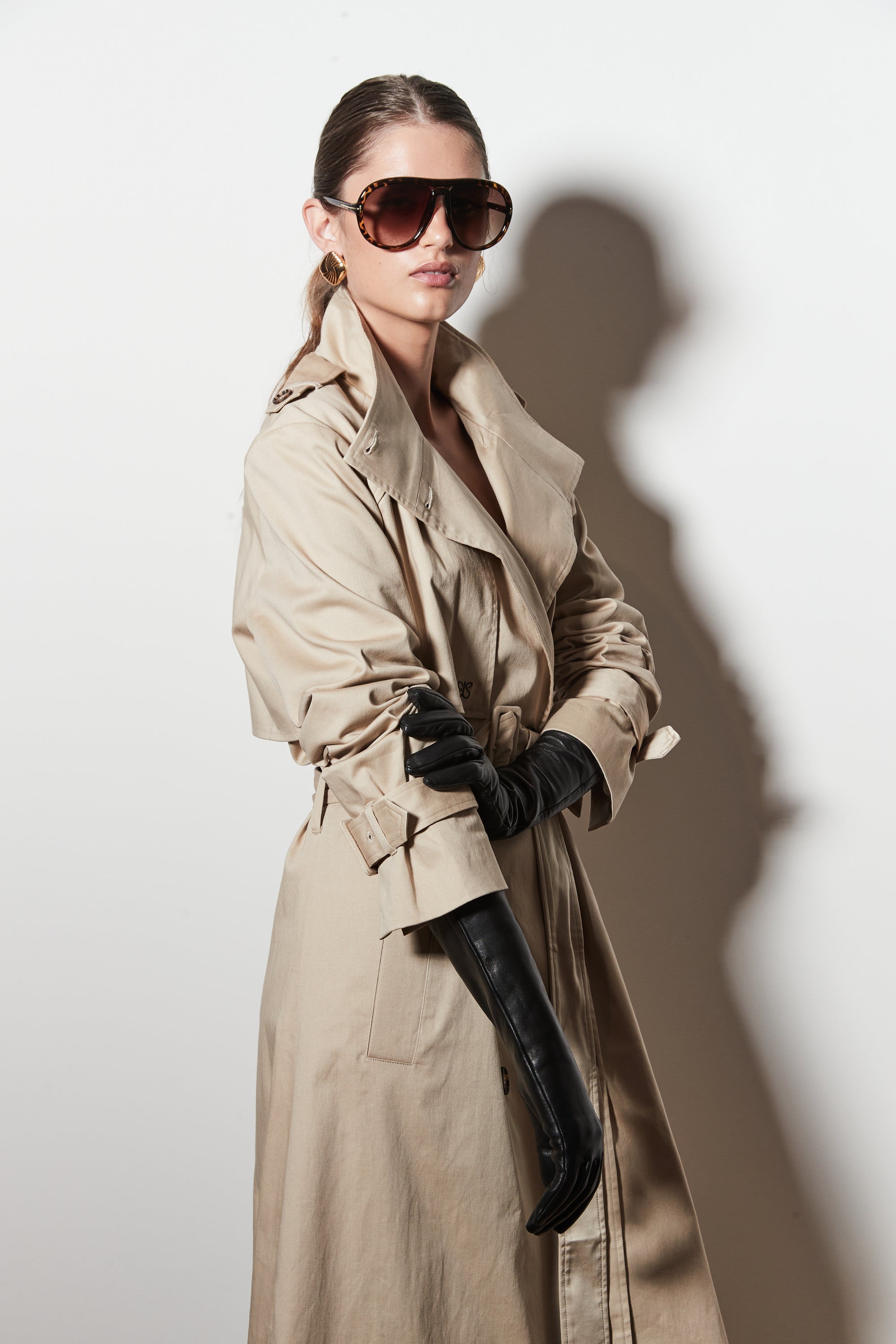 Woman wearing a beige trench coat, sunglasses, and black gloves