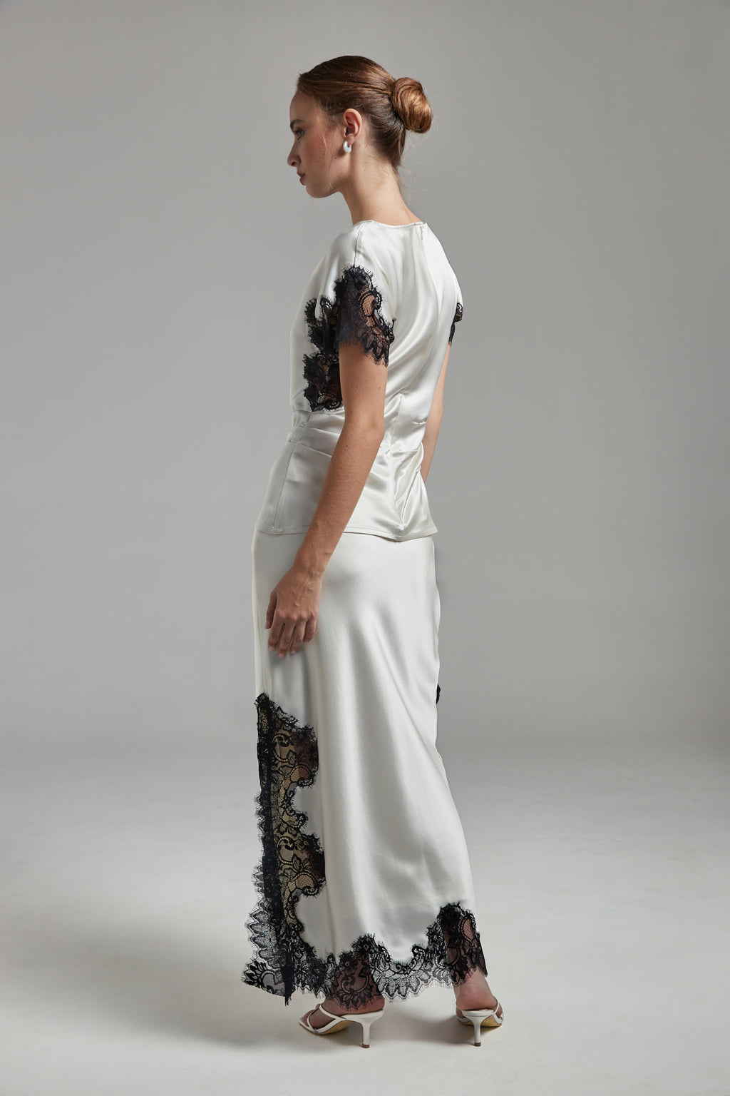 Model wearing the Anouk Maxi Skirt in Feather White with the Paloma Top, shown full-length from the back and side angle with black lace detailing and fluid silhouette.