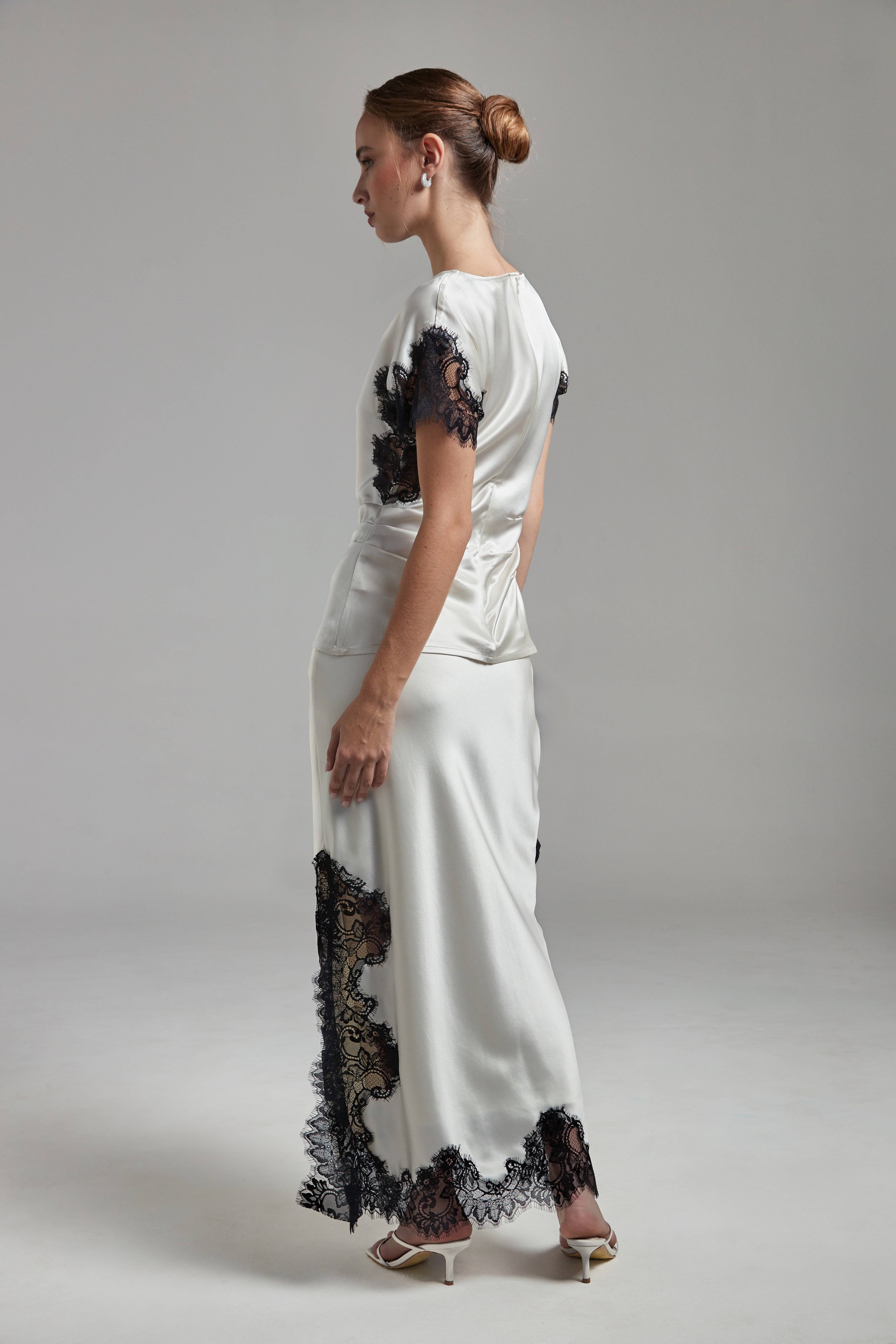 Model wearing the Anouk Maxi Skirt in Feather White with the Paloma Top, shown full-length from the back and side angle with black lace detailing and fluid silhouette.