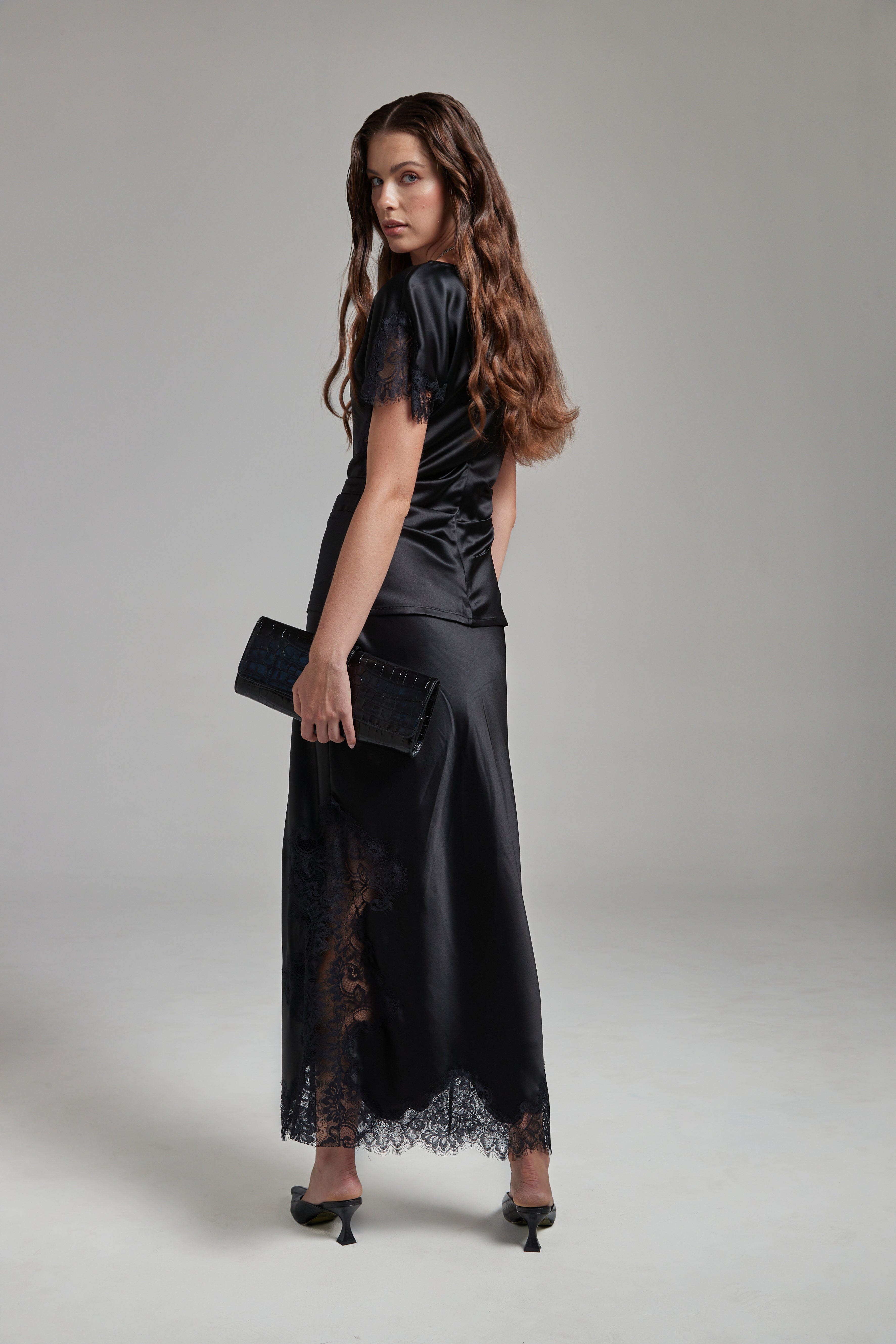 Model wearing the Anouk Maxi Skirt in Midnight Black with the Paloma Top, shown full-length from the back with black lace detailing and fluid silhouette.