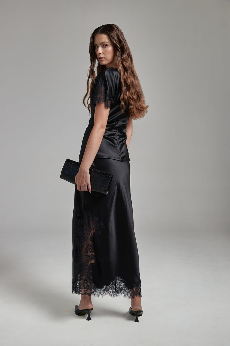 Model wearing the Anouk Maxi Skirt in Midnight Black with the Paloma Top, shown full-length from the back with black lace detailing and fluid silhouette.
