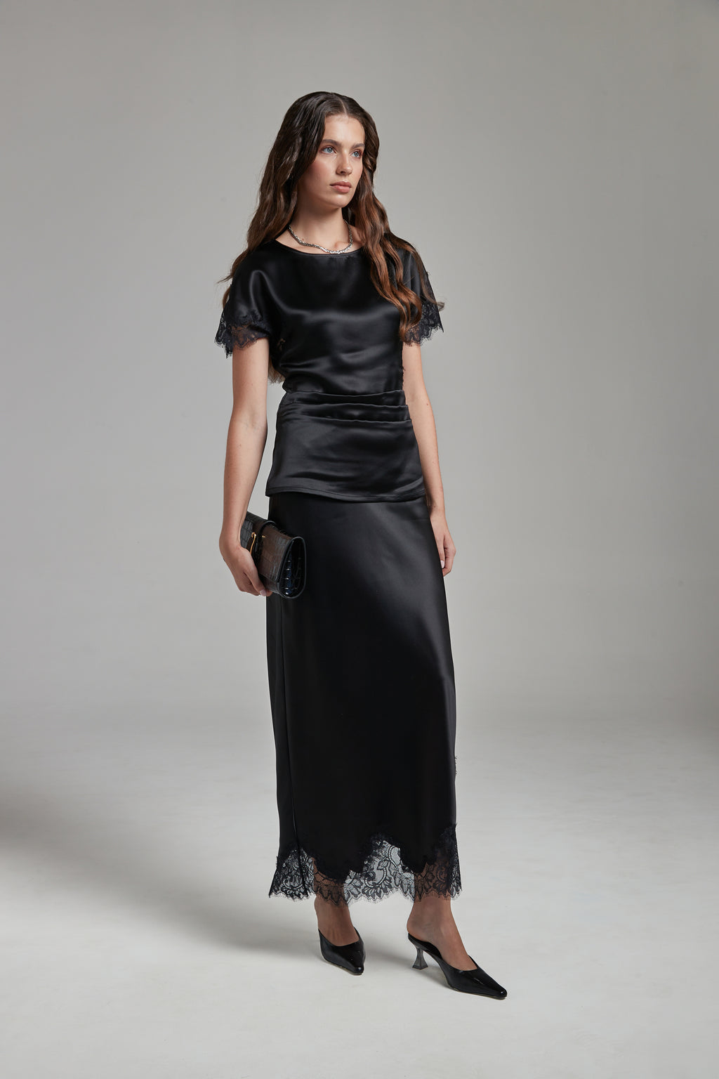 The Anouk Maxi Skirt in Midnight Black, a satin lace skirt shown full-length from the front with tonal lace trim and ankle-length silhouette.