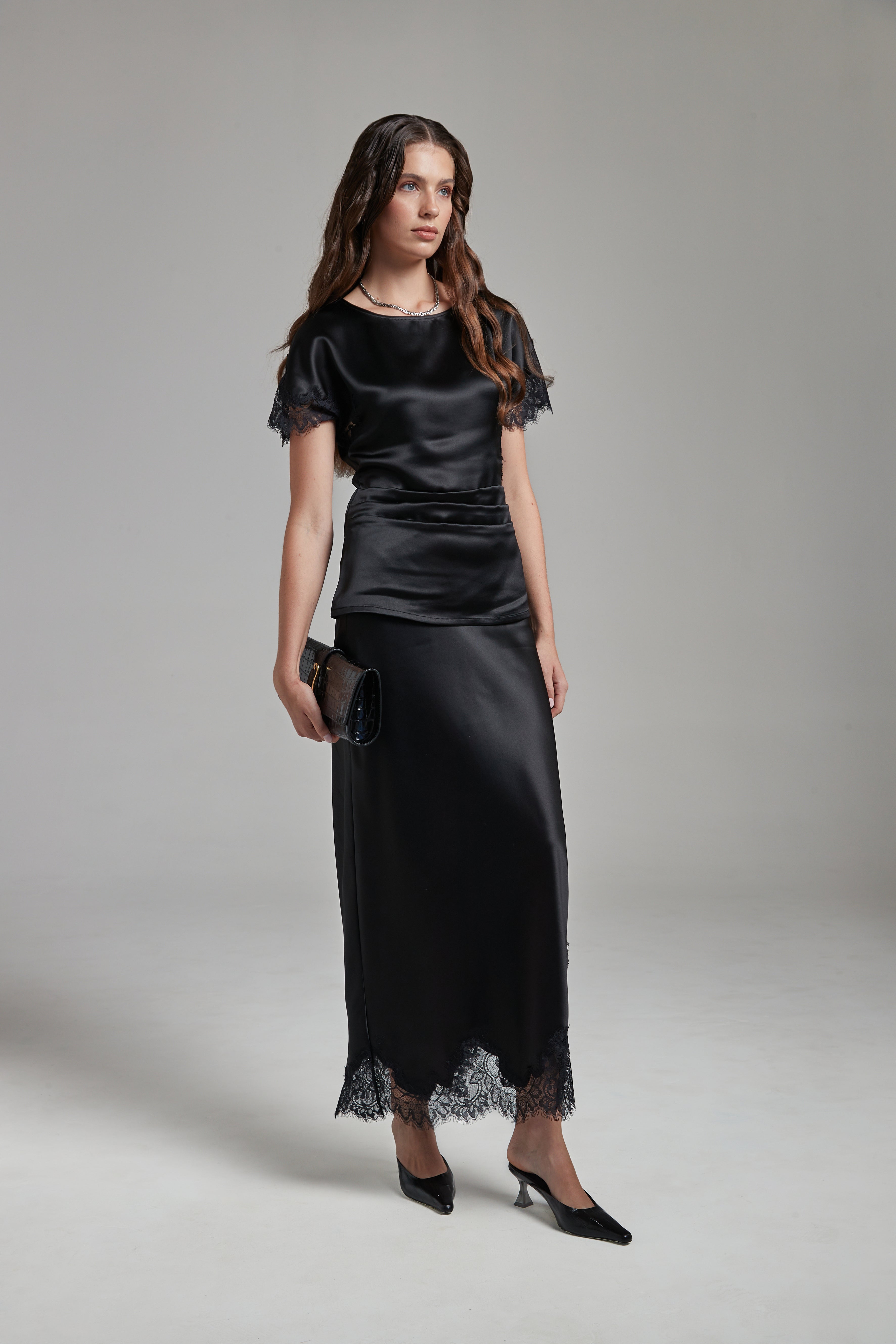 The Anouk Maxi Skirt in Midnight Black, a satin lace skirt shown full-length from the front with tonal lace trim and ankle-length silhouette.