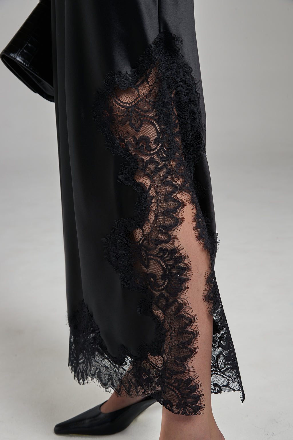 The Anouk Maxi Skirt in Midnight Black, a satin lace skirt shown close-up with tonal lace trim and side slit detail.