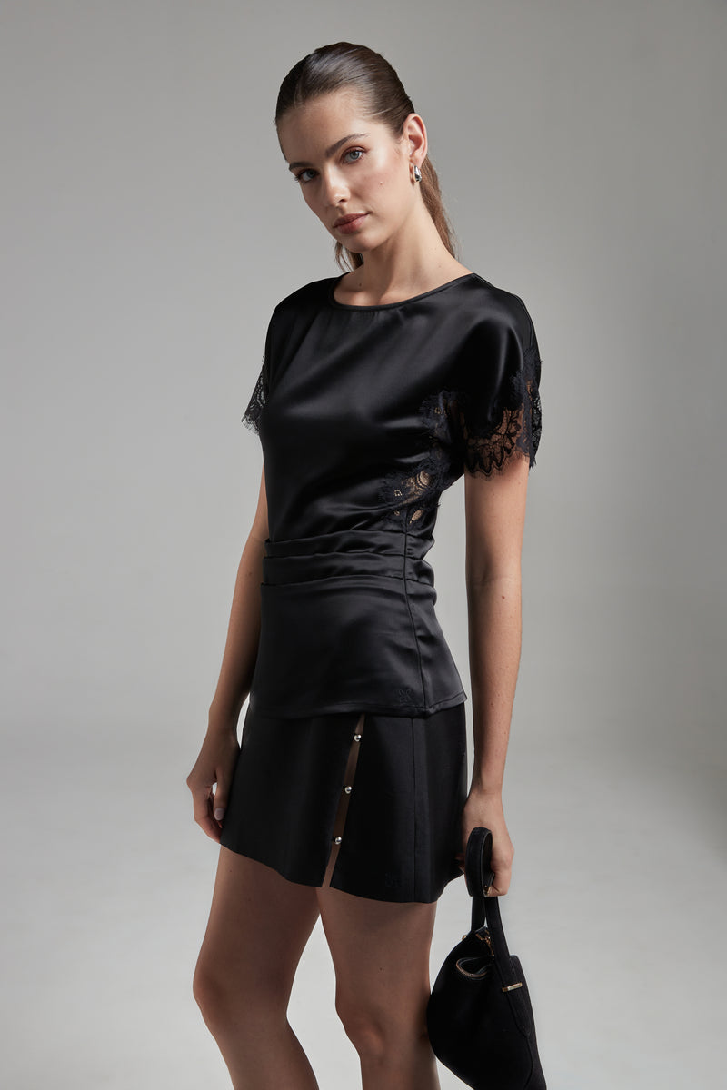 The Anya Mini Skirt in Midnight Black, a wool-silk mini skirt shown full-length from the side angle with a faux-wrap silhouette and side slit detail.