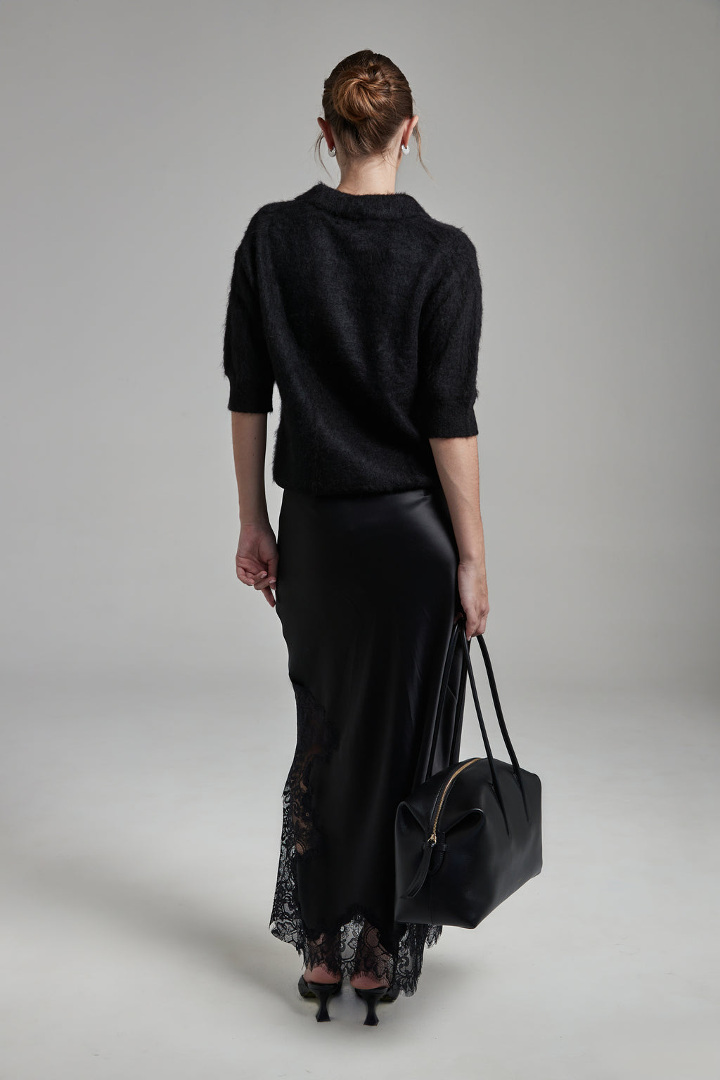Model wearing the Stella Polo Knit and Anouk Maxi Skirt in Feather White, shown full-length from the back with a brushed alpaca-blend knit and black lace trim detailing.