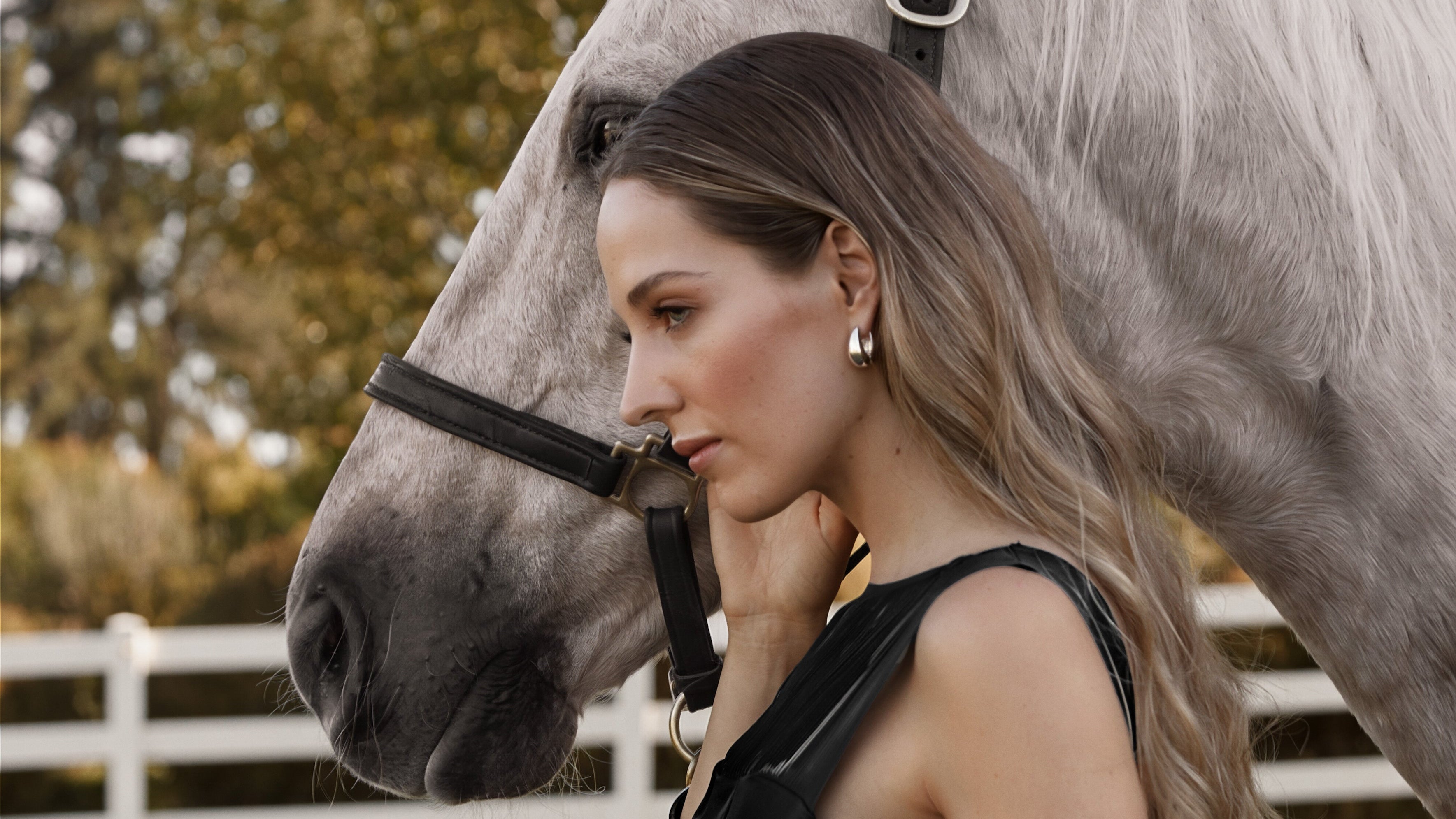 Woman in a black dress standing next to a palomino horse in an outdoor setting