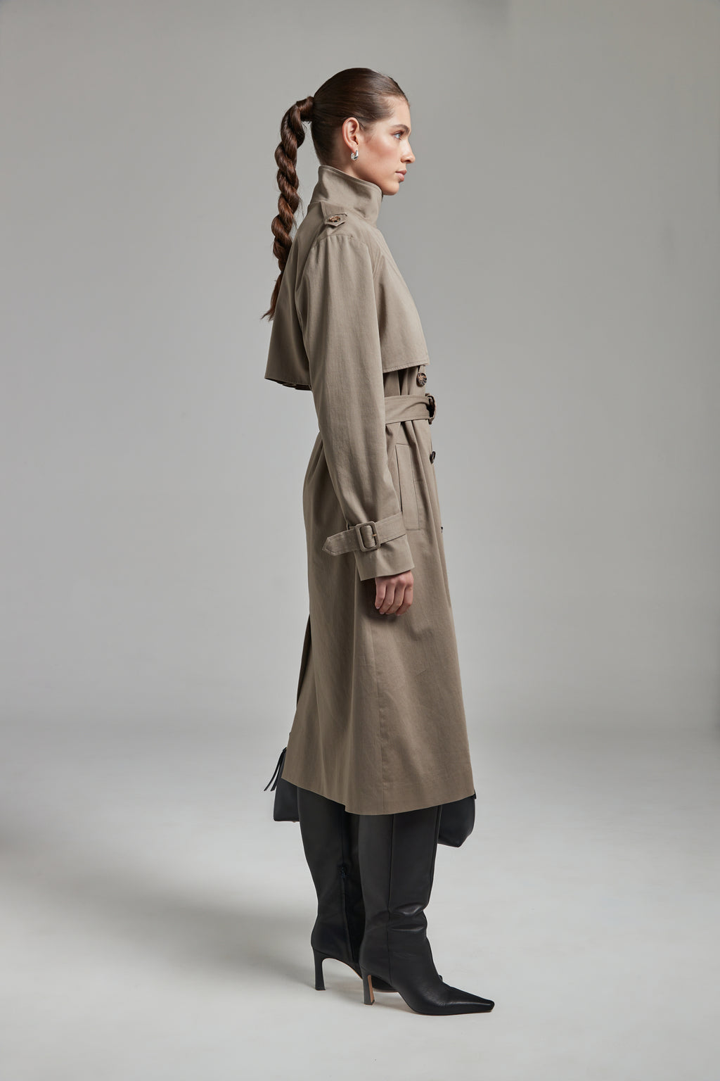 The Celeste Trench Coat in Desert Taupe shown full-length from the side with a funnel neckline and structured outerwear silhouette.