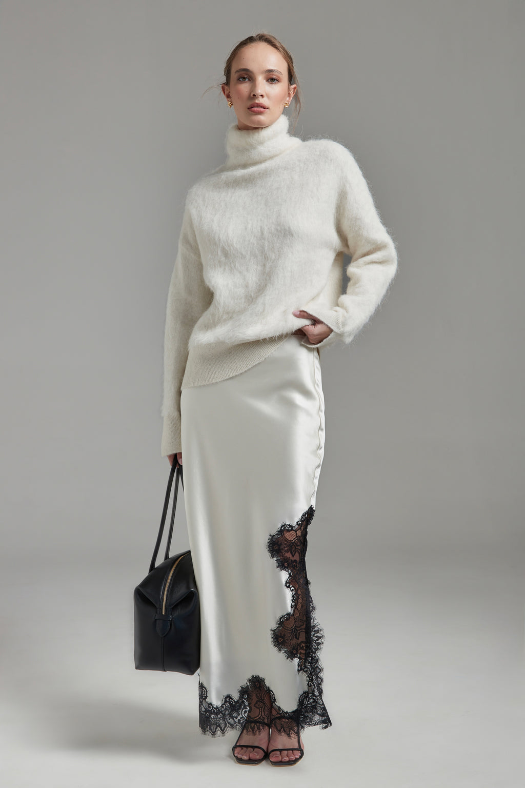 Model wearing the Lauren Turtleneck and Anouk Maxi Skirt in Feather White, shown full-length from the front with a brushed alpaca-blend knit and black lace trim.