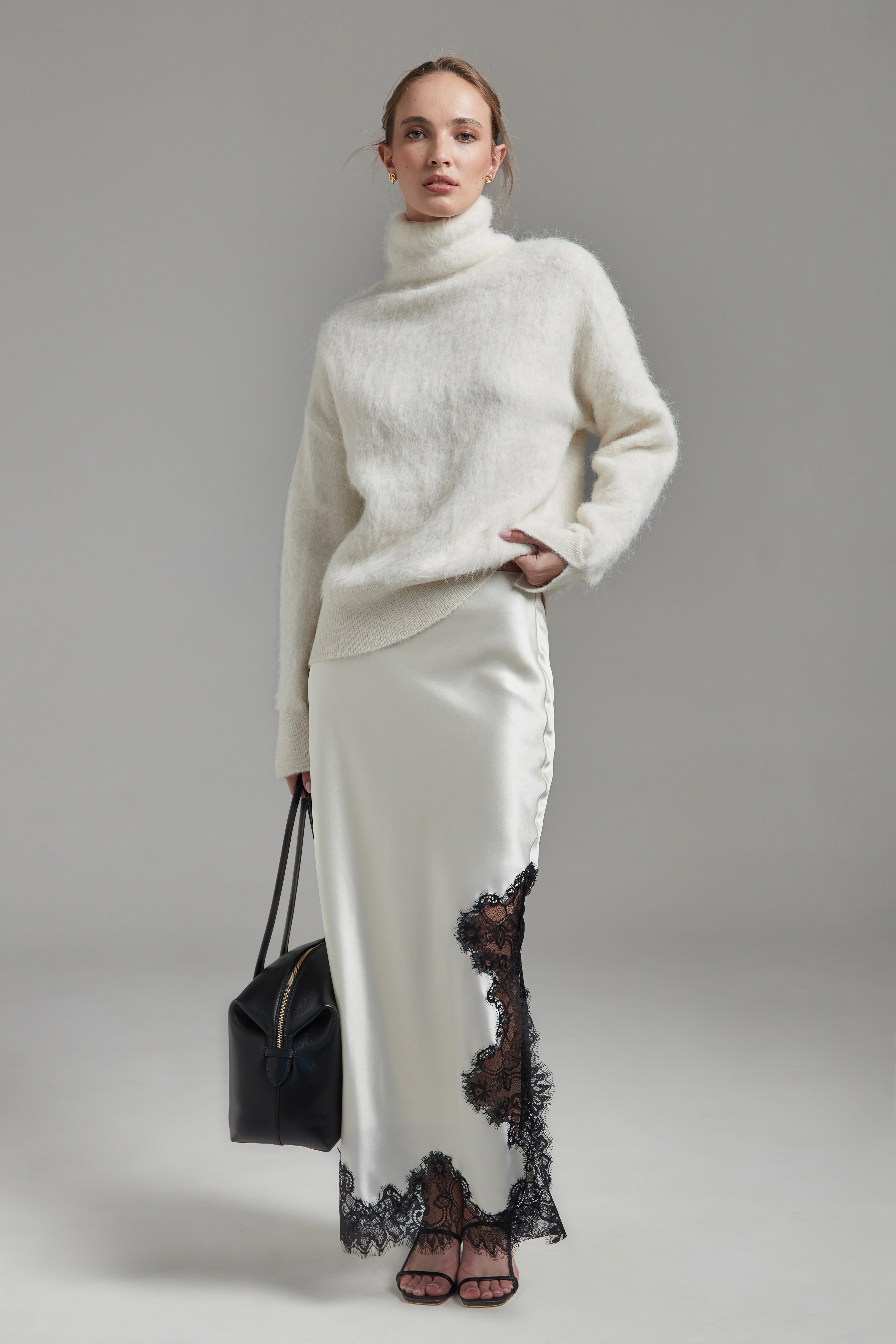 Model wearing the Lauren Turtleneck and Anouk Maxi Skirt in Feather White, shown full-length from the front with a brushed alpaca-blend knit and black lace trim.