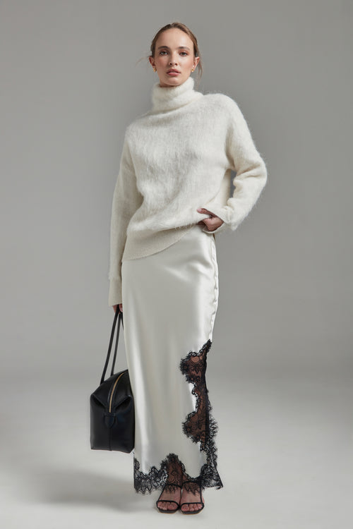 Model wearing the Lauren Turtleneck and Anouk Maxi Skirt in Feather White, shown full-length from the front with a brushed alpaca-blend knit and black lace trim.