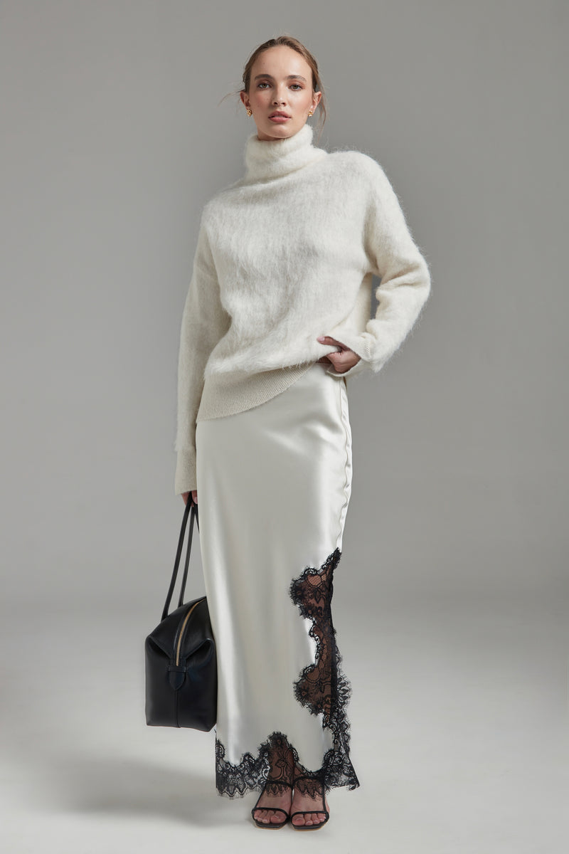 Model wearing the Lauren Turtleneck and Anouk Maxi Skirt in Feather White, shown full-length from the front with a brushed alpaca-blend knit and black lace trim.