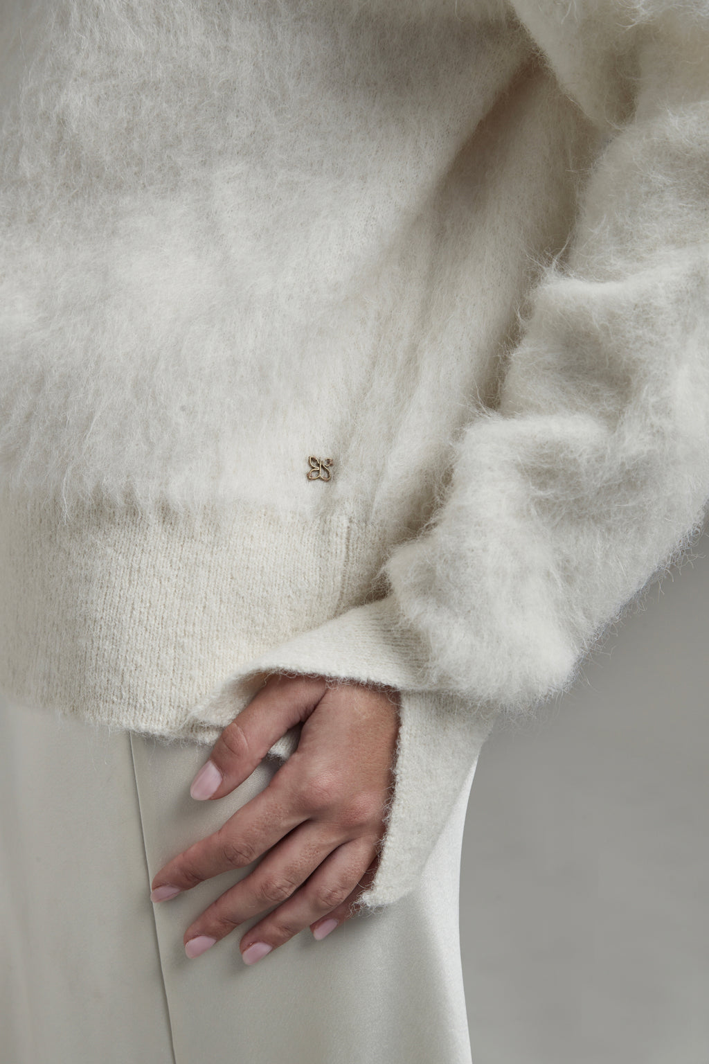 The Lauren Turtleneck in Feather White shown close-up with metal logo hardware detail and a brushed alpaca-blend texture.