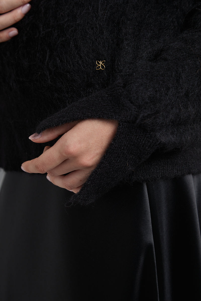 The Lauren Turtleneck in Midnight Black shown close-up with metal logo hardware detail and a brushed alpaca-blend texture.