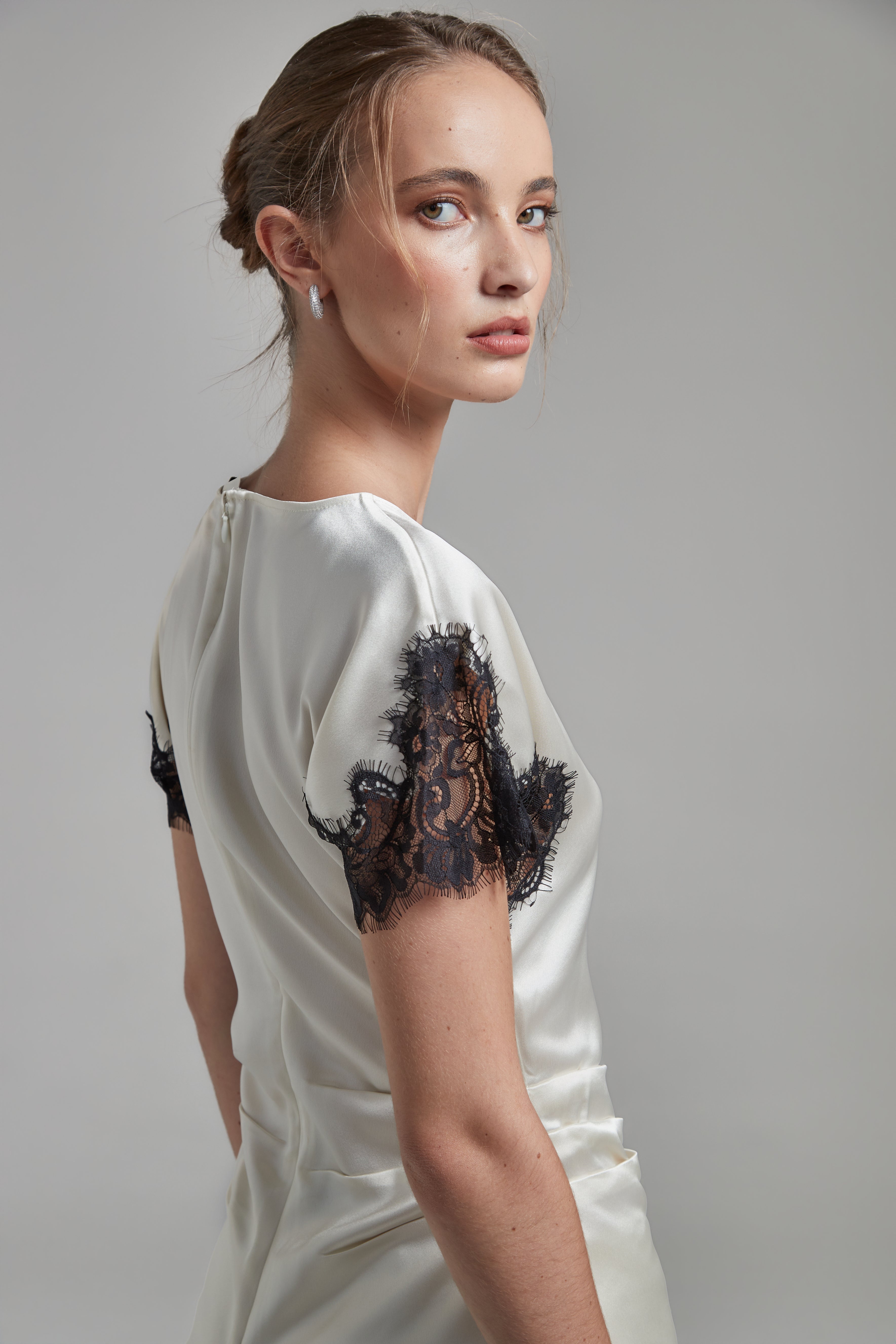 The Paloma Top in Feather White, a satin lace panel top shown from the side with black lace sleeve detailing and fitted silhouette.