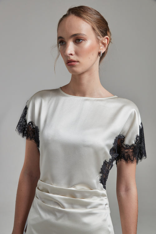 The Paloma Top in Feather White shown close-up from the side with a satin finish, black lace panel detailing and a fitted silhouette.