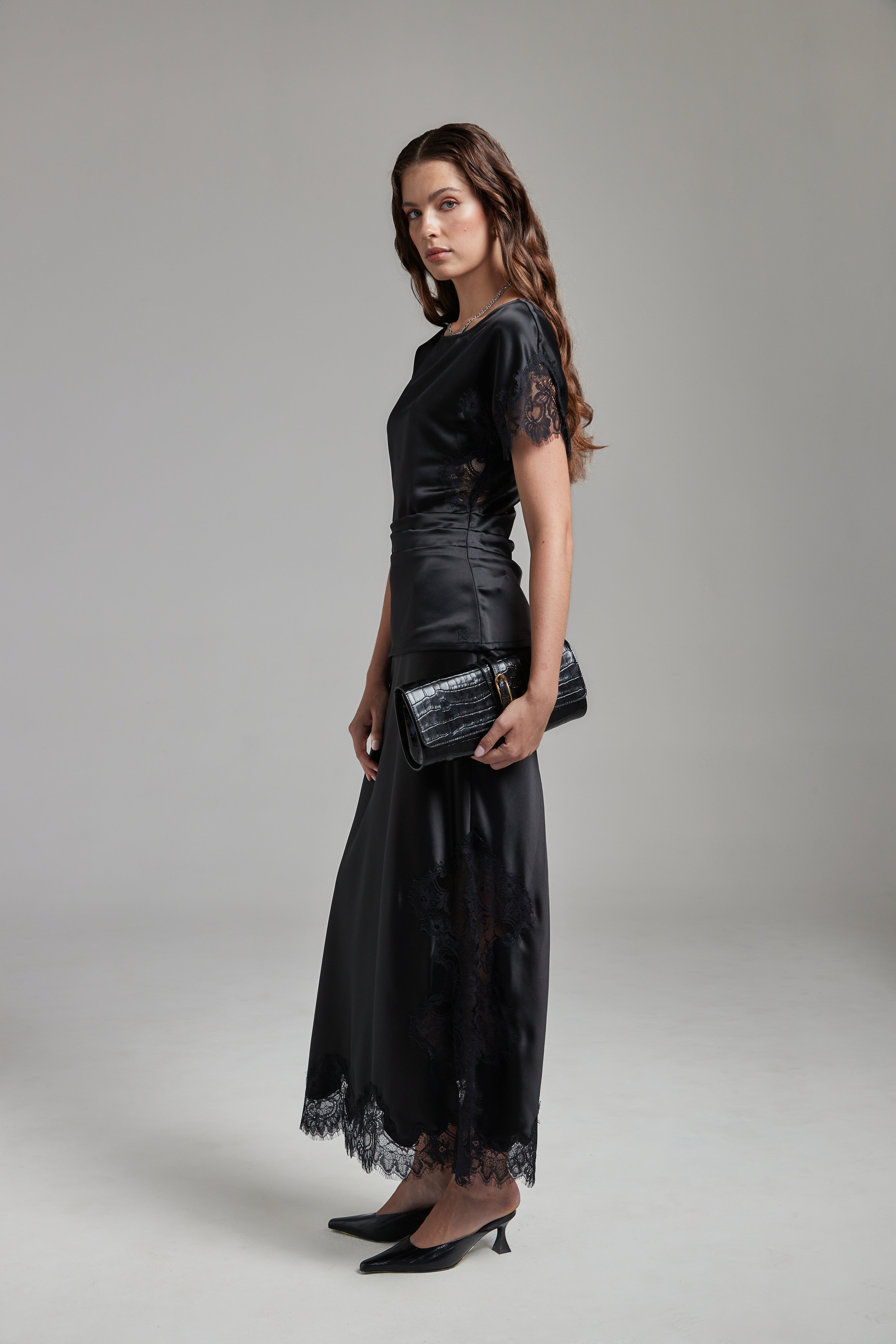 Model wearing the Paloma Top in Midnight Black with the Anouk Maxi Skirt, shown full-length from the side with tonal lace detailing and a fluid silhouette.