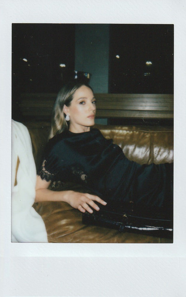 Polaroid-style photo of a woman sitting on a couch in a dimly lit room.
