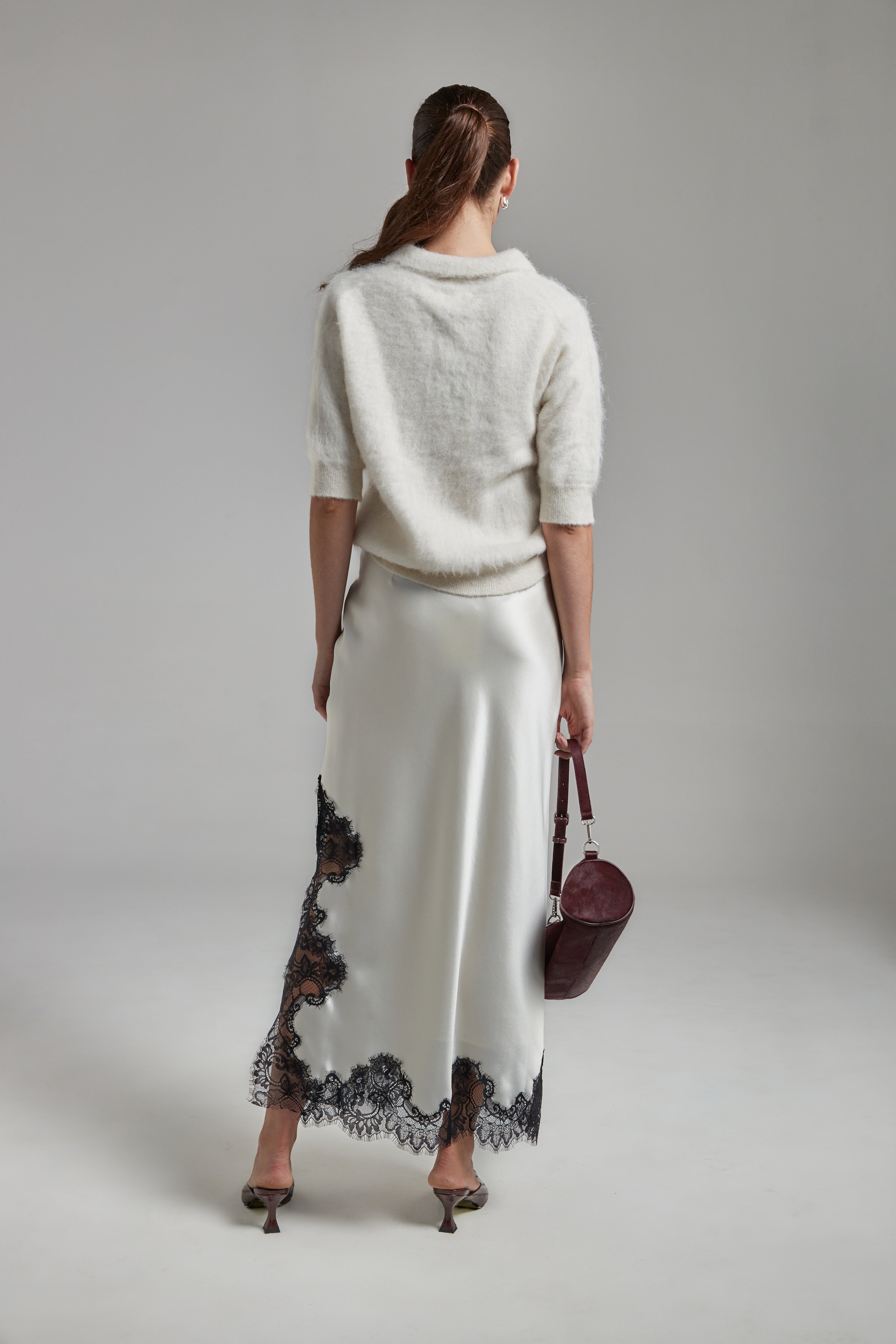 Model wearing the Stella Polo Knit and Anouk Maxi Skirt in Feather White, shown full-length from the back with a brushed alpaca-blend knit and black lace trim detailing.
