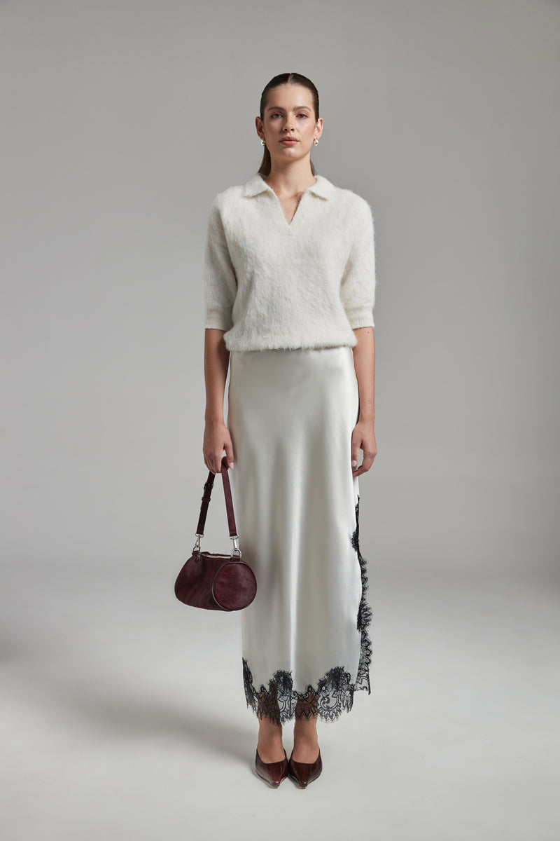 Model wearing the Stella Polo Knit and Anouk Maxi Skirt in Feather White, shown full-length from the front with an alpaca-blend knit and satin skirt with black lace trim.