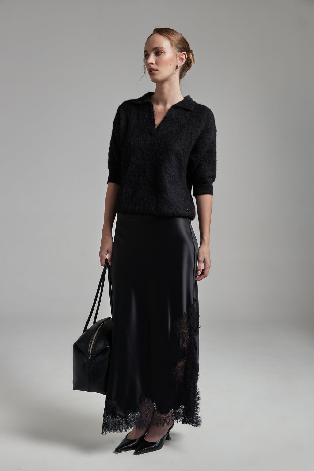 Model wearing the Stella Polo Knit and Anouk Maxi Skirt in Midnight Black, shown full-length with a brushed alpaca-blend knit and satin skirt with black lace trim.