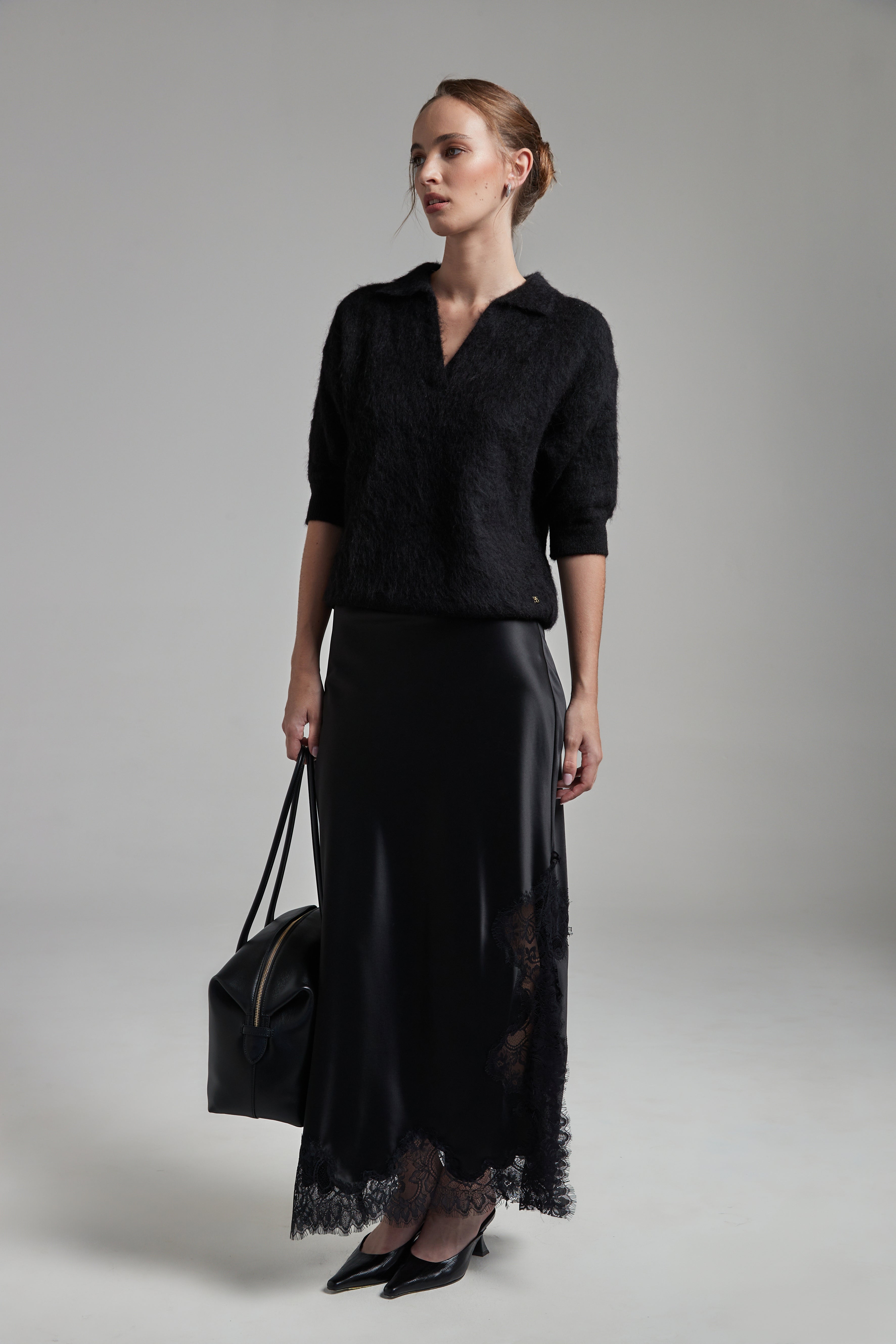 Model wearing the Stella Polo Knit and Anouk Maxi Skirt in Midnight Black, shown full-length with a brushed alpaca-blend knit and satin skirt with black lace trim.