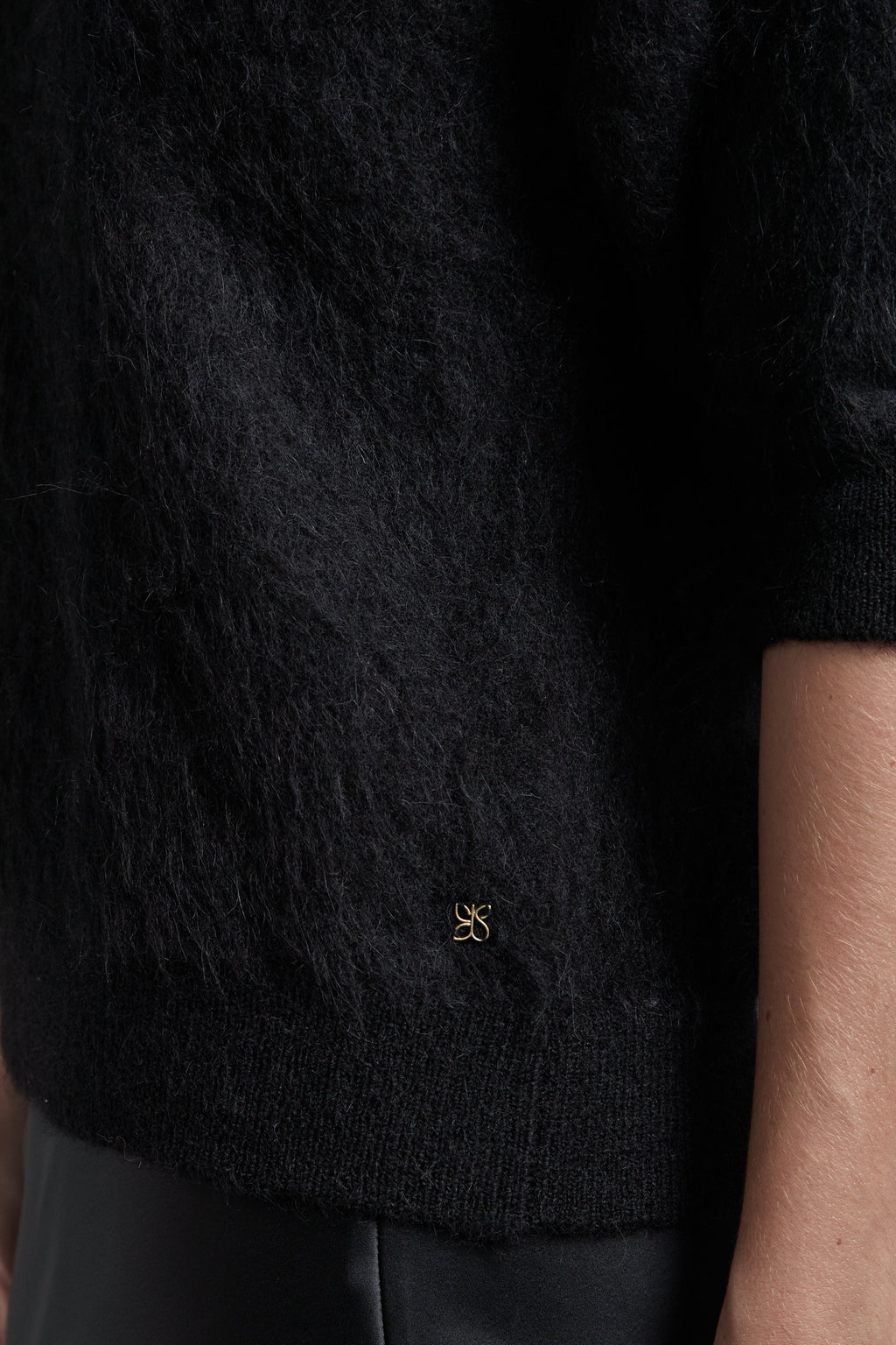 The Stella Polo Knit in Midnight Black shown close-up with brushed alpaca-blend texture and metal logo hardware detail.